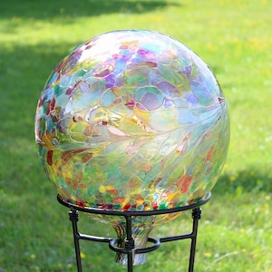May include: A colorful glass gazing ball with a mosaic-like pattern in shades of green, yellow, red, and purple. The decorative sphere sits on a black metal stand, perfect for garden decor. The ball has a diameter of approximately 10 inches.