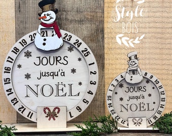 May include: Wooden Christmas countdown calendar with a snowman and the text "JOURS jusqu'à NOËL". The calendar is circular with numbers around the edge and a small stand. The snowman has a black hat and red scarf. The calendar measures approximately 20 cm in diameter.