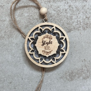 May include: A round wooden ornament with a cutout design and the text "Style Bois" inside. The ornament is attached to a brown twine string.