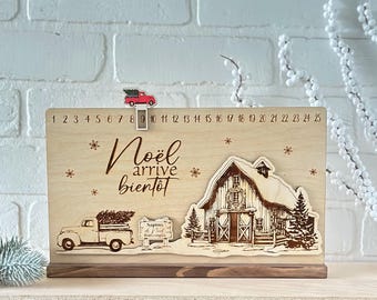 May include: Wooden advent calendar featuring a red truck, a Christmas tree, and a farmhouse scene. The calendar has numbers 1 to 25 and the text "Noël arrive bientôt".
