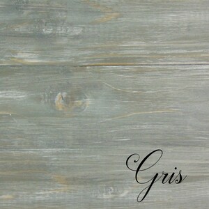 Op de afbeelding: Een close-up van een verweerd grijs houten oppervlak met het woord "Gris" geschreven in zwarte cursieve letters.