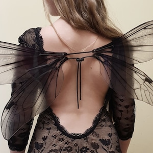 Puede incluir: Una mujer con un vestido de encaje negro con la espalda descubierta y alas de mariposa negras transparentes.
