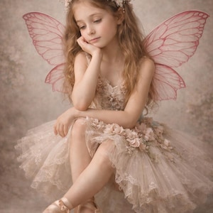 May include: A young person dressed as a fairy, wearing a floral crown, pink wings, and a tutu adorned with flowers. The fairy is seated, resting their chin on their hand, with ballet slippers on their feet.