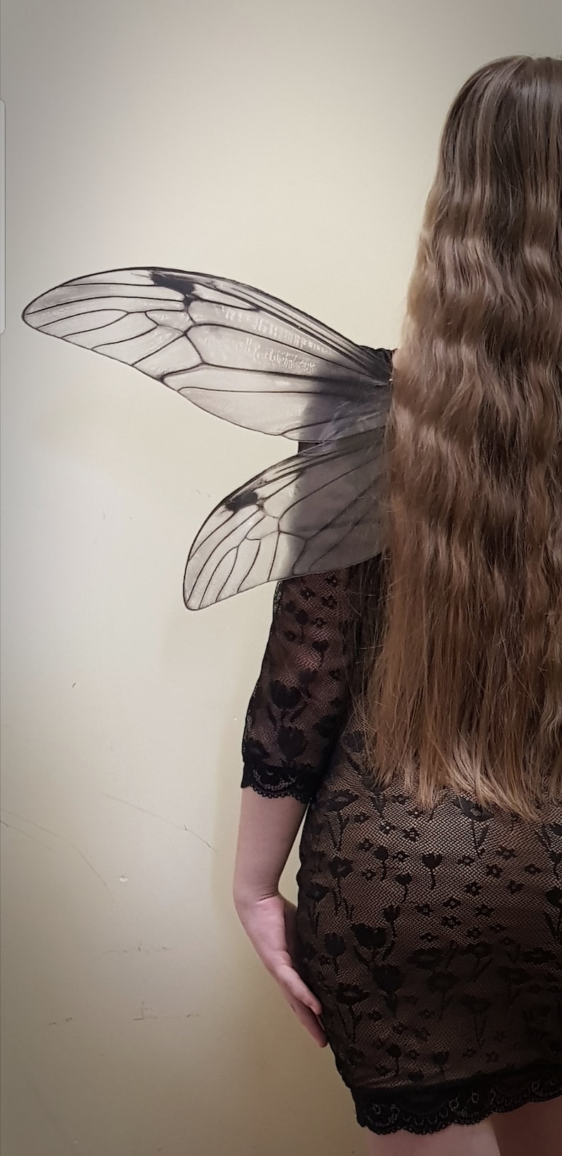 Puede incluir: Una persona con un vestido de encaje negro y un par de alas de insecto grandes y transl&uacute;cidas unidas a su espalda.