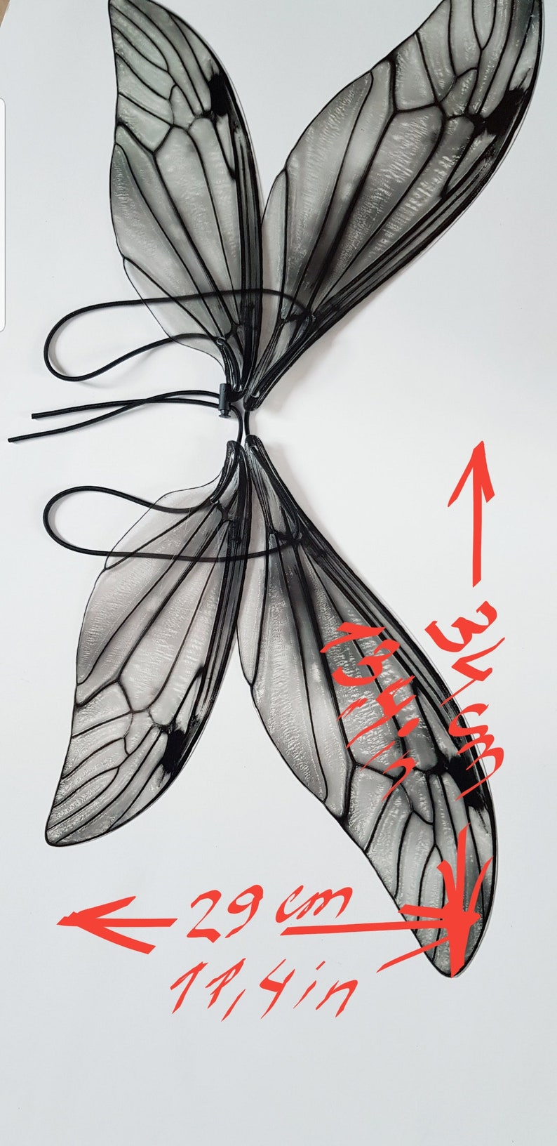 Puede incluir: Alas de mariposa negras y blancas con una textura transparente y ligera. Las alas est&aacute;n unidas a una banda el&aacute;stica negra. Las alas miden 74 cm de ancho y 84 cm de alto.