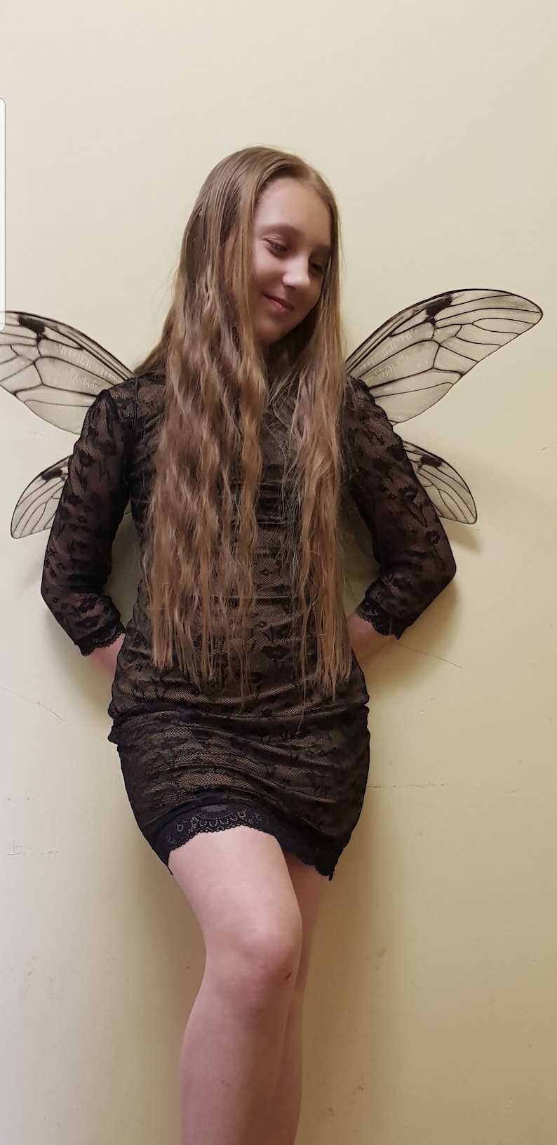 Puede incluir: Una persona joven con un vestido de encaje negro y un par de alas de insecto grandes y transl&uacute;cidas.