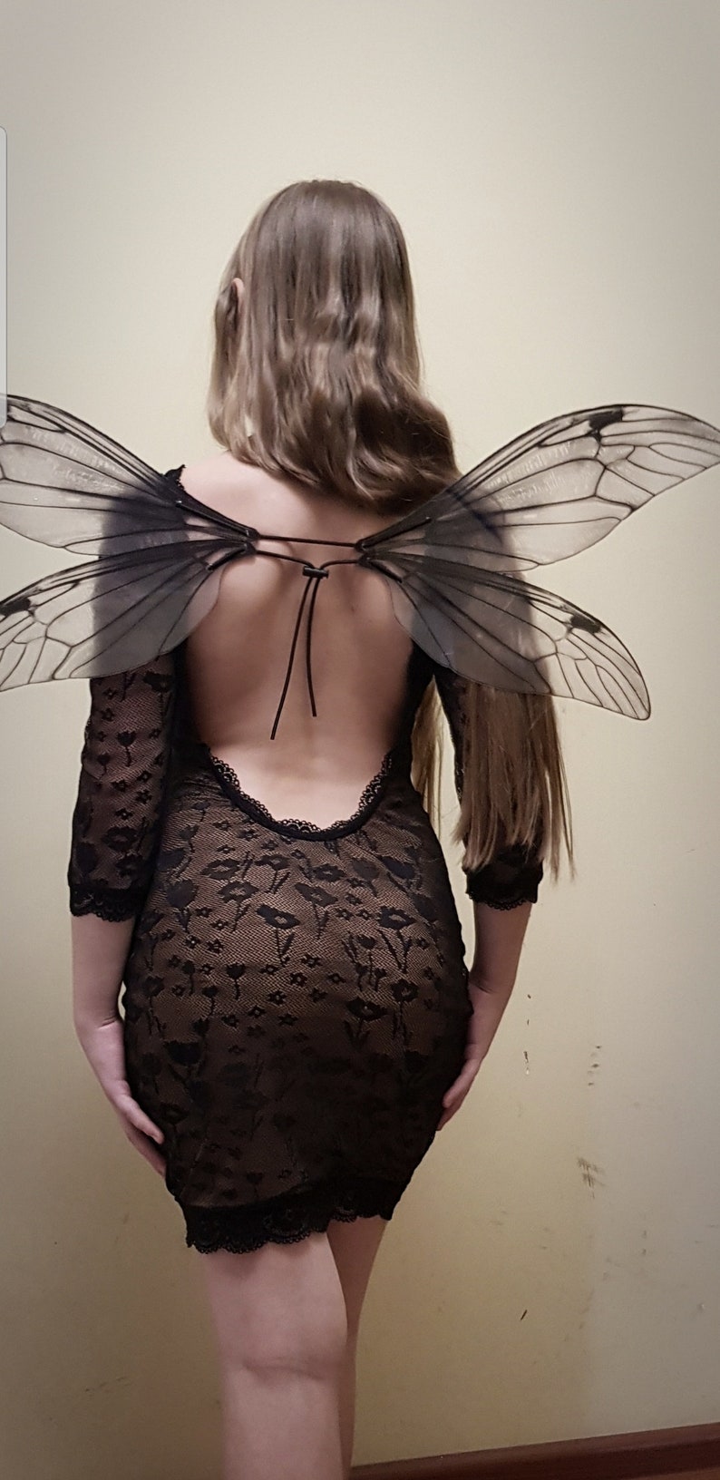 Puede incluir: Una mujer con un vestido negro de encaje con la espalda descubierta y un par de alas grandes, negras y transl&uacute;cidas.