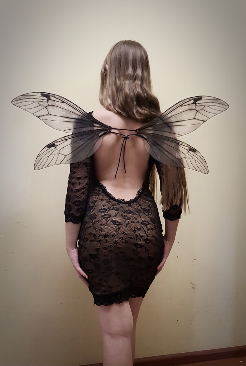 Puede incluir: Una persona con un vestido negro de encaje con la espalda descubierta y un par de alas grandes, negras, de insecto.