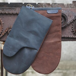 May include: Two oven mitts, one dark blue and one brown, hanging on a rusty metal chain and gear mechanism. The dark blue mitt has a leather texture and the brown mitt has a canvas texture. The brown mitt has the word "GOODAITY" printed on it.