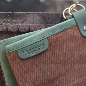 May include: A brown canvas pouch with a green leather trim and a metal clasp. The pouch has a label that reads "POHVALIN Handcrafted Ltd. Finland".