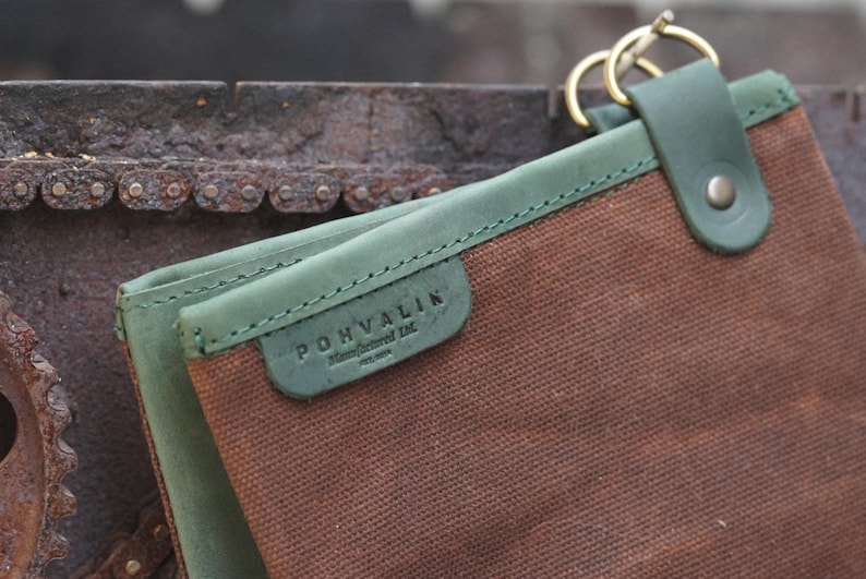 May include: A brown canvas pouch with a green leather trim and a metal clasp. The pouch has a label that reads "POHVALIN Handcrafted Ltd. Finland".