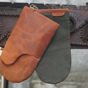 May include: A pair of oven mitts, one brown leather and one green canvas, hanging from a metal chain.