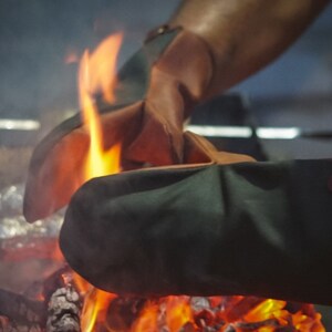 May include: A pair of heat-resistant oven mitts, one green and one brown, are being used to hold a piece of foil over a glowing fire.