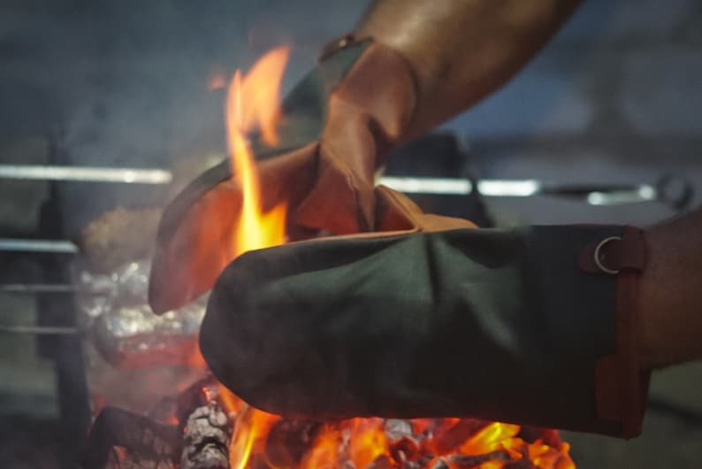 May include: A pair of heat-resistant oven mitts, one green and one brown, are being used to hold a piece of foil over a glowing fire.