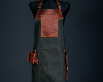 May include: A dark green canvas apron with brown leather straps and pockets. The apron has a large brown leather patch on the front with the word "MADE" embossed on it.