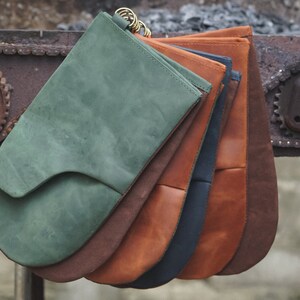 May include: A set of five leather oven mitts in various colors, including green, brown, orange, navy blue, and tan. The mitts are stacked on top of each other and are hanging from a metal chain.