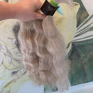 May include: A bundle of wavy, light blonde human hair extensions with a brown label that reads "Indian Hair".