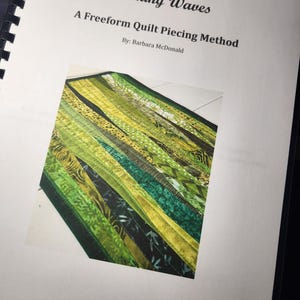 May include: A spiral-bound instructional booklet titled Making Waves: A Freeform Quilt Piecing Method by Barbara McDonald. The cover features a photograph of a quilt made from various green fabric strips with diverse patterns and textures.
