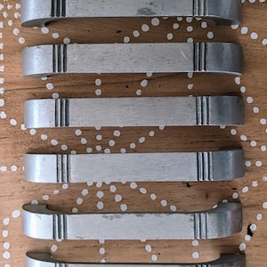 May include: Six silver metal cabinet drawer pulls with a decorative design. The pulls are arranged vertically on a wooden surface with white polka dots.