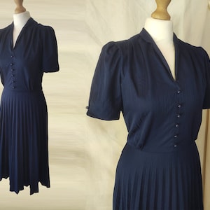 May include: A navy blue dress with a pleated skirt and short sleeves. The dress has a V-neckline and a button closure down the front.