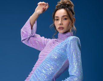 May include: A woman wearing a sequined dress with a purple and blue color scheme. The dress has a high neck and long sleeves.