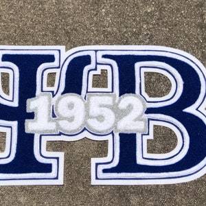 Pode incluir: Um remendo de feltro azul e branco com as letras "ΨΒ" e o ano "1952" em branco.