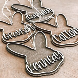 May include: Four wooden bunny-shaped ornaments with the names Grayson, Camden, Colton, and Kennedy written in white on them.