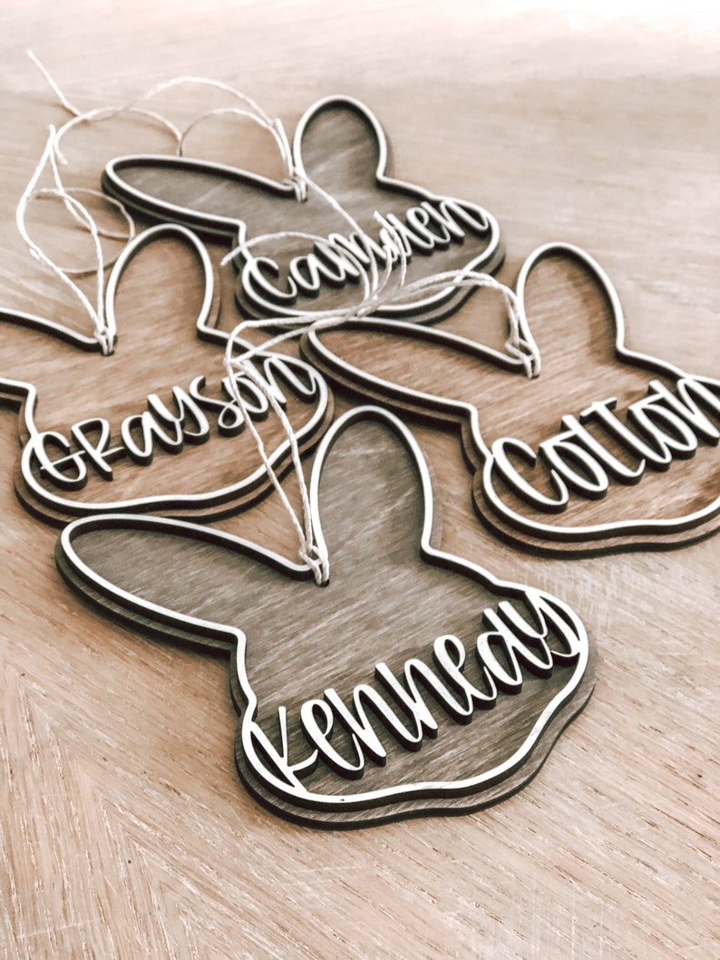 May include: Four wooden bunny-shaped ornaments with the names Grayson, Camden, Colton, and Kennedy written in white on them.
