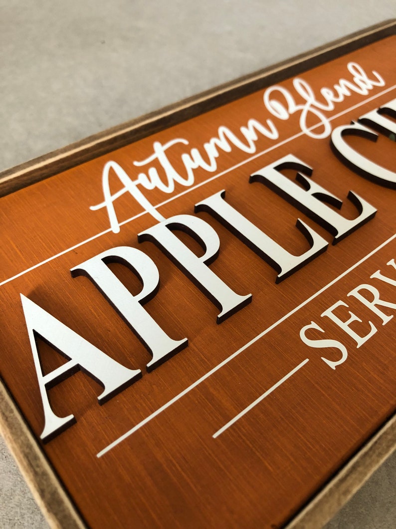 Peut inclure: Une enseigne en bois avec un fond brun et du texte blanc. L'enseigne indique "Autumn Blend Apple Cider" et "Serving".