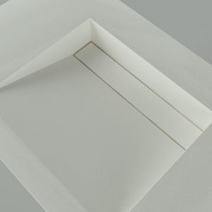 May include: A minimalist, abstract composition featuring a white, folded paper structure. The design incorporates a recessed rectangular area with subtle linear details, creating a sense of depth and shadow play. The overall aesthetic is clean and modern.
