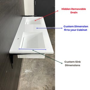 May include: A white double sink vanity with a rectangular design. The vanity features two square sinks and is supported by black metal brackets. Text on the image indicates custom dimensions and a hidden removable drain.