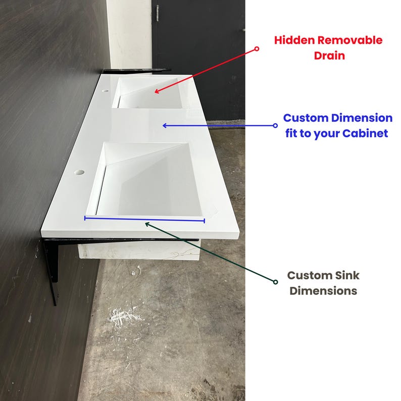 May include: A white double sink vanity with a rectangular design. The vanity features two square sinks and is supported by black metal brackets. Text on the image indicates custom dimensions and a hidden removable drain.