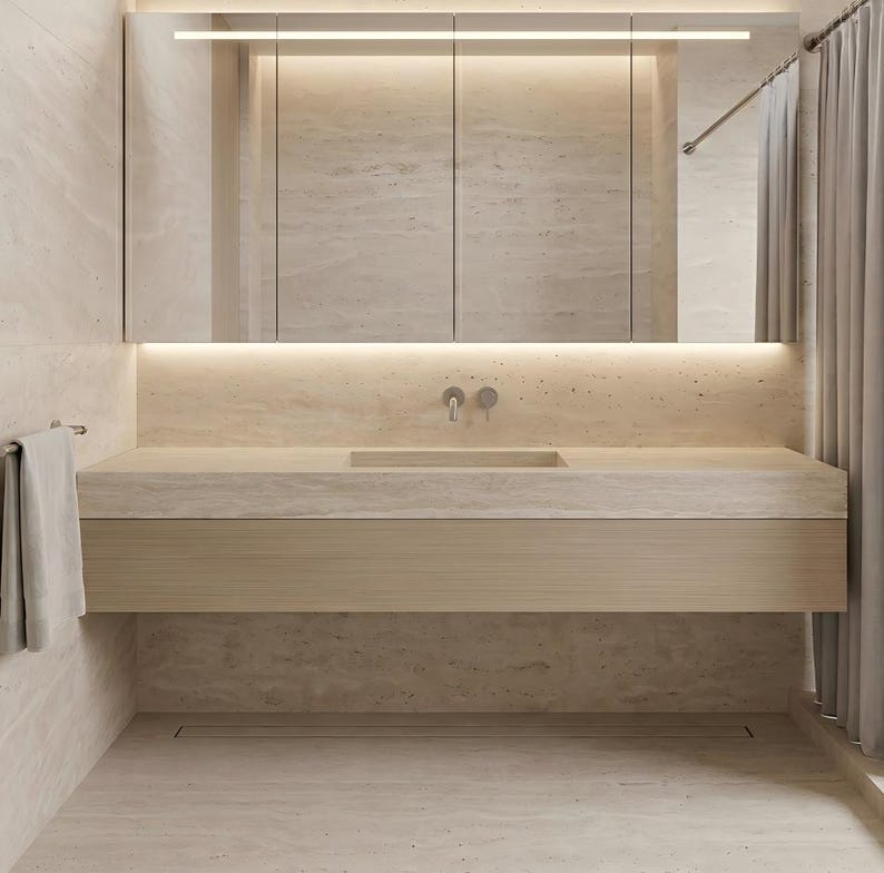 Puede incluir: Un mueble de ba&ntilde;o con encimera de piedra beige claro y lavabo integrado, montado sobre un armario horizontal de madera clara. Un gran armario con espejo de tres paneles e iluminaci&oacute;n LED integrada se sit&uacute;a sobre el lavabo.
