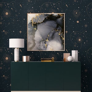 Op de afbeelding: Een donkergroene kast met gouden accenten staat voor een donkerblauwe muur met een gouden en wit sterrenhemelpatroon. Een ingelijst abstract schilderij met grijze en gouden swirls hangt boven de kast.