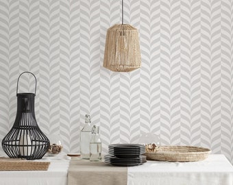 May include: A white and gray chevron patterned wallpaper with a woven pendant light hanging from the ceiling. A table with a white tablecloth is set with a black woven lantern, two clear glass bottles, a stack of black plates, and a woven basket.