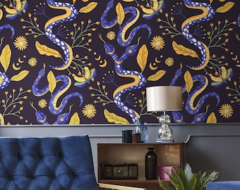 Puede incluir: Un sillón de terciopelo azul con un marco de metal dorado se encuentra en una sala de estar con un papel tapiz estampado con serpientes, lunas y flores. Un jarrón de flores rosas se encuentra en una mesa de café frente al sillón.