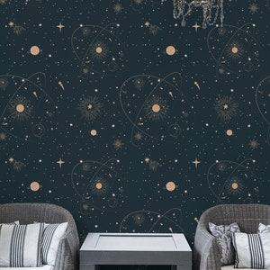Op de afbeelding: Twee rieten fauteuils met witte kussens staan ​​tegenover elkaar aan een zwarte salontafel. De muur achter de meubels is bedekt met donkerblauw behang met een gouden sterrenhemelpatroon van sterren, planeten en sterrenbeelden.