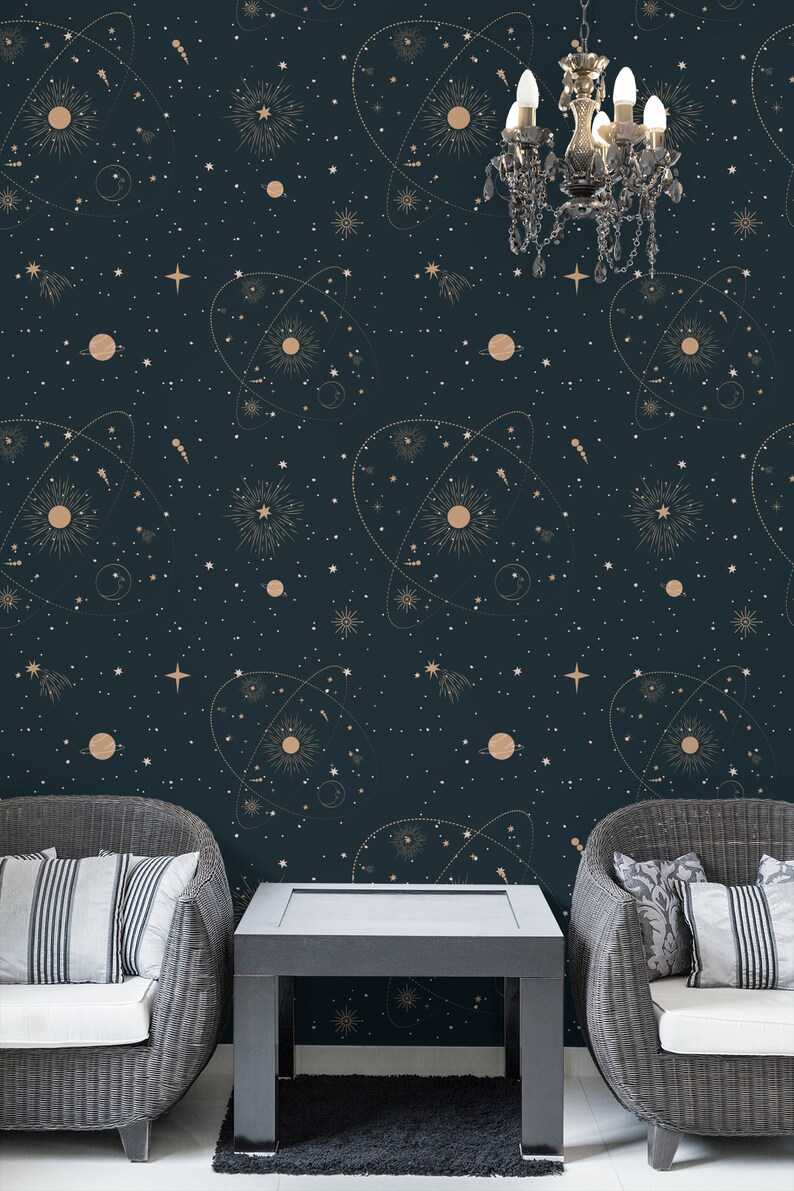 Op de afbeelding: Twee rieten fauteuils met witte kussens staan ​​tegenover elkaar aan een zwarte salontafel. De muur achter de meubels is bedekt met donkerblauw behang met een gouden sterrenhemelpatroon van sterren, planeten en sterrenbeelden.