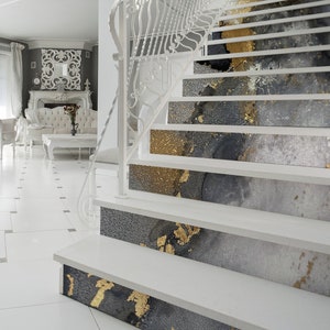 Puede incluir: Escalera blanca con un patr&oacute;n abstracto dorado y gris en cada escal&oacute;n. Los escalones son de madera y tienen un acabado blanco. La escalera est&aacute; en una casa moderna con pisos de baldosas blancas.