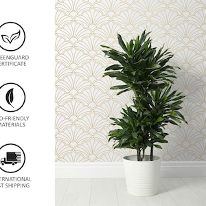 Op de afbeelding: Een groene plant in een pot met meerdere stengels en bladeren in een witte pot tegen een witte muur met een gouden geometrisch patroon. De plant staat in een witte pot met een textuur.