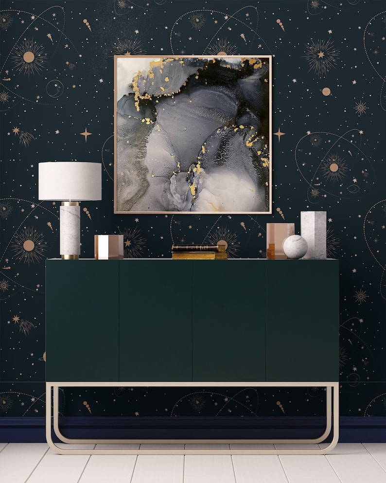 Op de afbeelding: Een donkergroene kast met gouden accenten staat voor een donkerblauwe muur met een gouden en wit sterrenhemelpatroon. Een ingelijst abstract schilderij met grijze en gouden swirls hangt boven de kast.