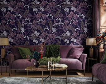 May include: A purple velvet sofa with green velvet throw pillows sits in front of a wall with a floral wallpaper pattern. The wallpaper features a dark purple background with white and light purple flowers. A coffee table with a marble top sits in front of the sofa.