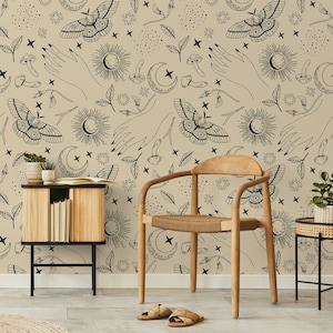 Può includere: Una sedia in legno con seduta intrecciata si trova davanti a un muro con sfondo beige e un motivo bianco e nero di stelle, lune, farfalle e mani.