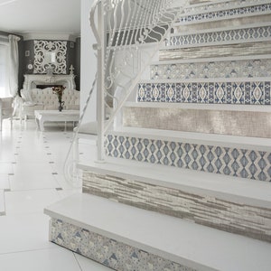 Könnte beinhalten: Weiße Treppe mit dekorativen Fliesenelementen in einem geometrischen Muster. Die Fliesen sind in Blautönen, Grau und Beige gehalten. Die Treppe befindet sich in einem modernen Haus mit weißen Wänden und einem weißen Fliesenboden.