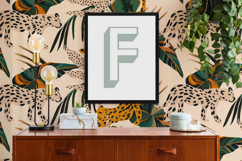 Peut inclure: Une impression encadr&eacute;e noire avec une lettre "F" vert clair sur fond blanc. L'impression est accroch&eacute;e &agrave; un mur avec un fond beige orn&eacute; d'un motif r&eacute;p&eacute;titif de l&eacute;opards stylis&eacute;s et de feuilles tropicales dans des tons de vert, orange et marron.