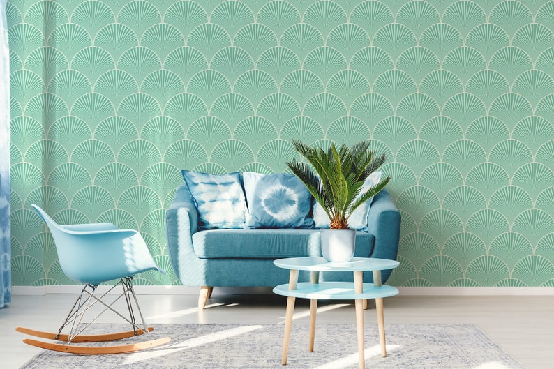 May include: A living room interior with a teal blue sofa, two blue throw pillows, a rocking chair, a potted plant, and a two-tiered light blue coffee table. The wall is covered in a teal green wallpaper with a white geometric pattern.