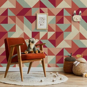 Può includere: Una carta da parati con motivo geometrico rosso, beige e verde con un decoro da parete a forma di coniglio in legno, una cornice in legno con il testo "Small steps every day", una poltrona in velluto marrone con una scimmia di peluche seduta su di essa e un cesto intrecciato con un coperchio marrone.