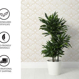Op de afbeelding: Een groene plant in een witte pot met een gouden en witte geometrische patroonbehang op de achtergrond.