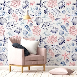 Può includere: Uno sfondo bianco con un motivo ripetitivo di conchiglie blu e rosse, stelle marine e coralli. Una poltrona rosa con un cuscino bianco è posizionata davanti al muro con il motivo.