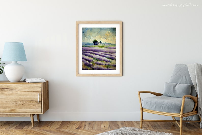 May include: A watercolor painting of a lavender field with a small tree in the distance. The sky is a light blue with white clouds. The painting is framed in a light wood frame.